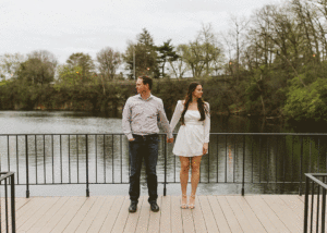 engaged couple near water holding hands and swinging them