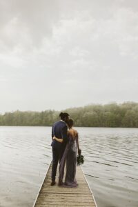 couple cozy up cuddling on the dock in the rain at long lake outdoor center for a wedding