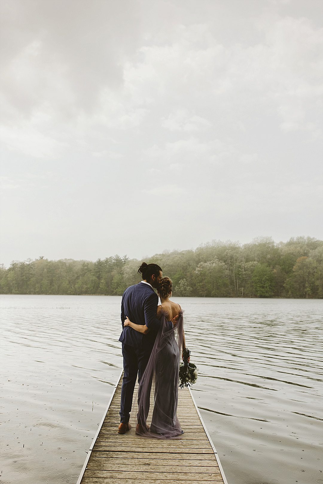 couple cozy up cuddling on the dock in the rain at long lake outdoor center for a wedding long-lake-outdoor-center-wedding
